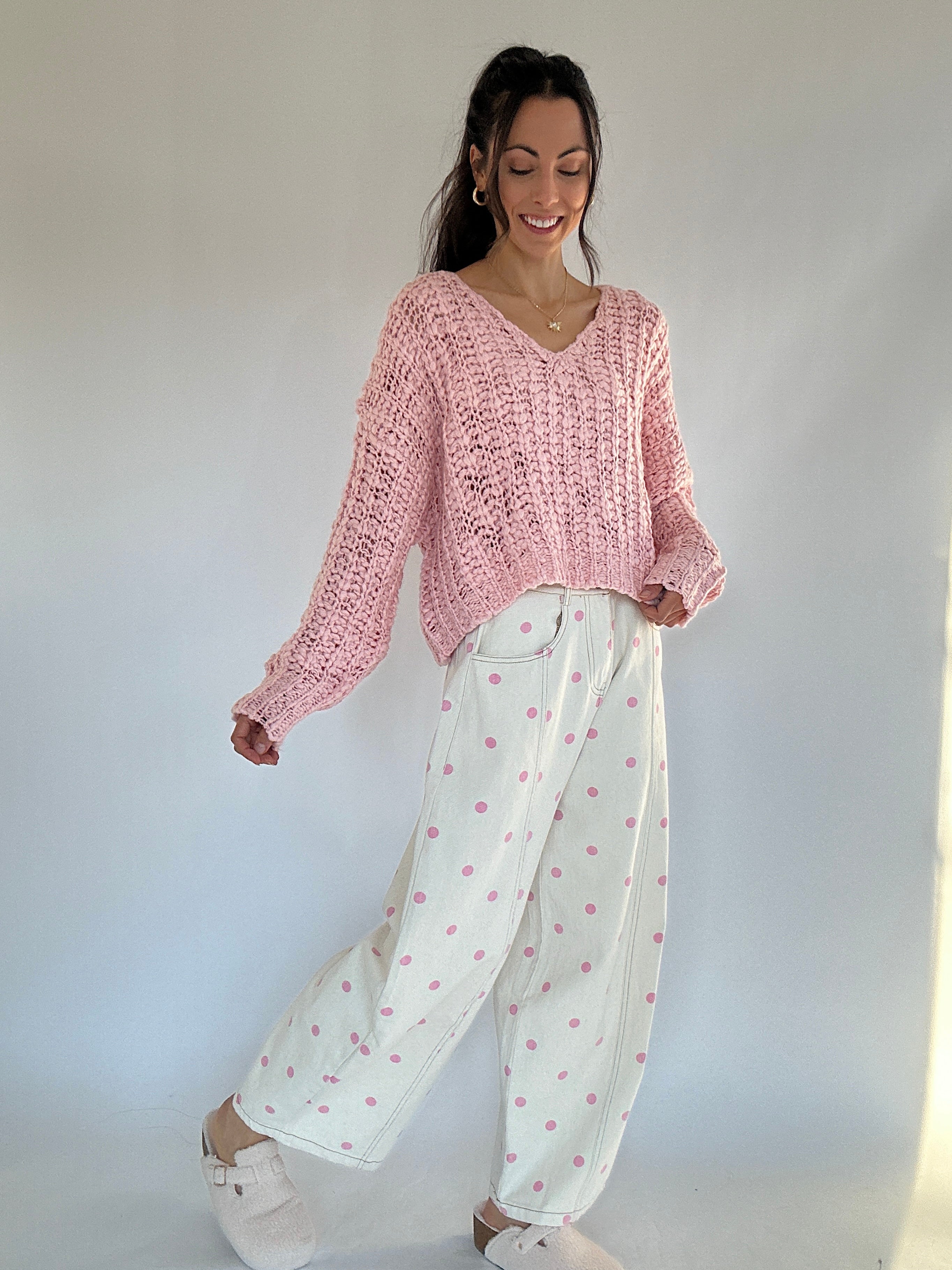 Woman wearing a pink knitted sweater and white pants with pink polka dots against a plain background