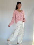 Woman wearing a pink knitted sweater and white pants with pink polka dots against a plain background