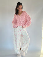 Woman wearing a pink knitted sweater and white pants with pink polka dot patterns against a plain background