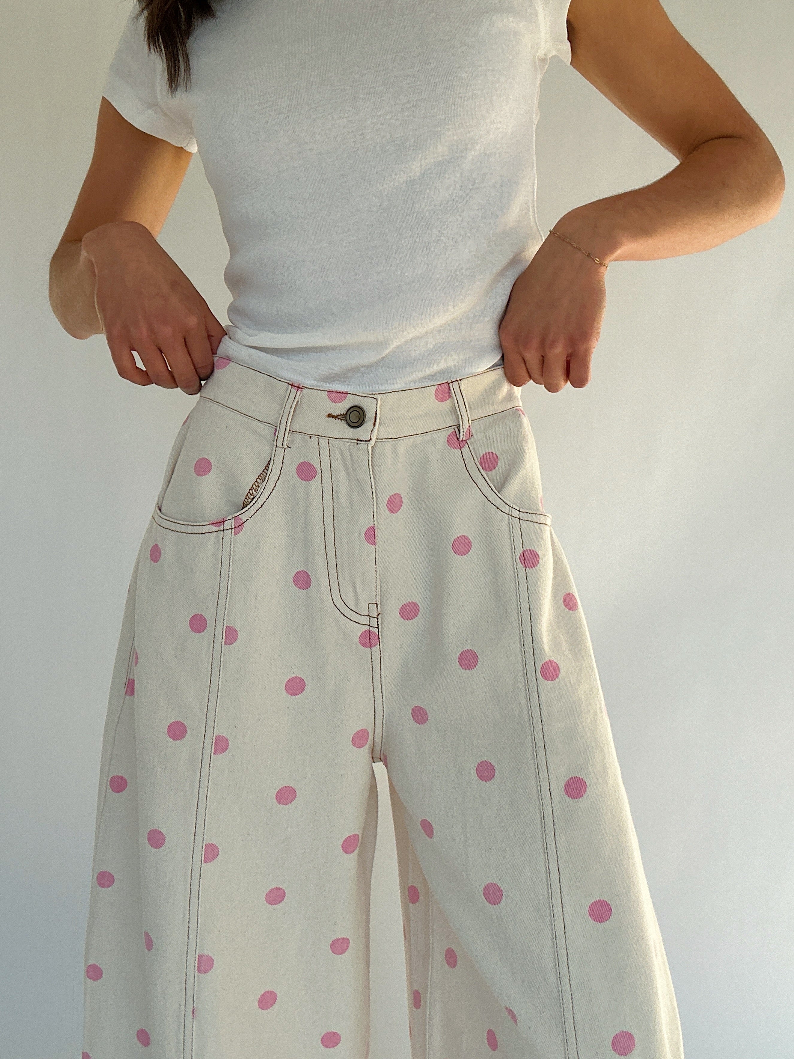 Person wearing a white t-shirt and white pants with pink polka dots against a plain background showing button and zip fly