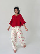 Woman wearing a red top and white pants with red polka dots on a plain background