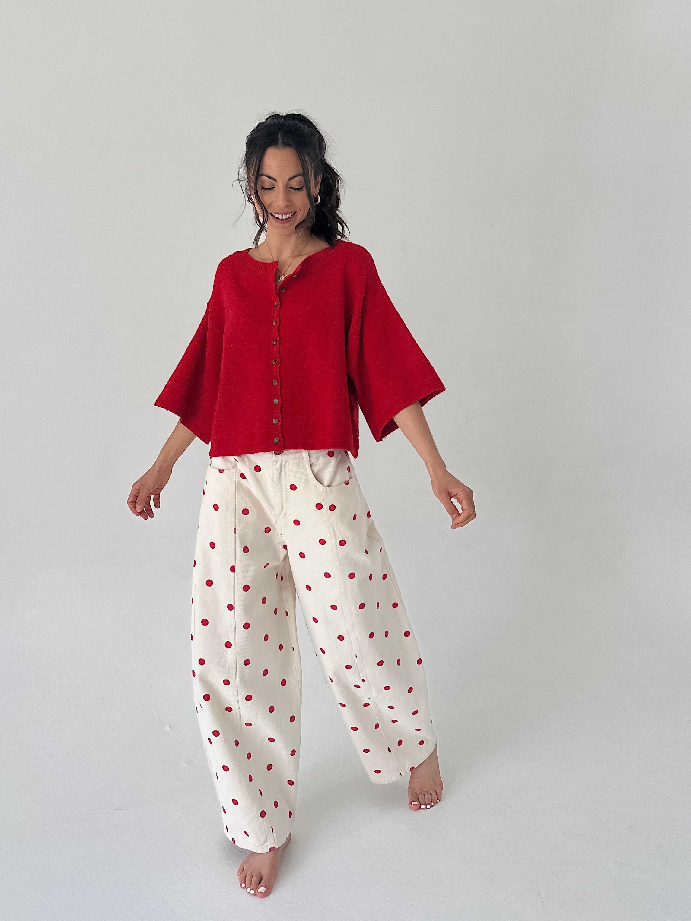 Woman wearing a red top and white pants with red polka dots on a plain background