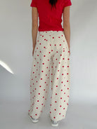 Person wearing a red top and white pants with red polka dots on a plain background from back