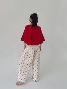 Person wearing a red top and white pants with red polka dots on a plain background from back
