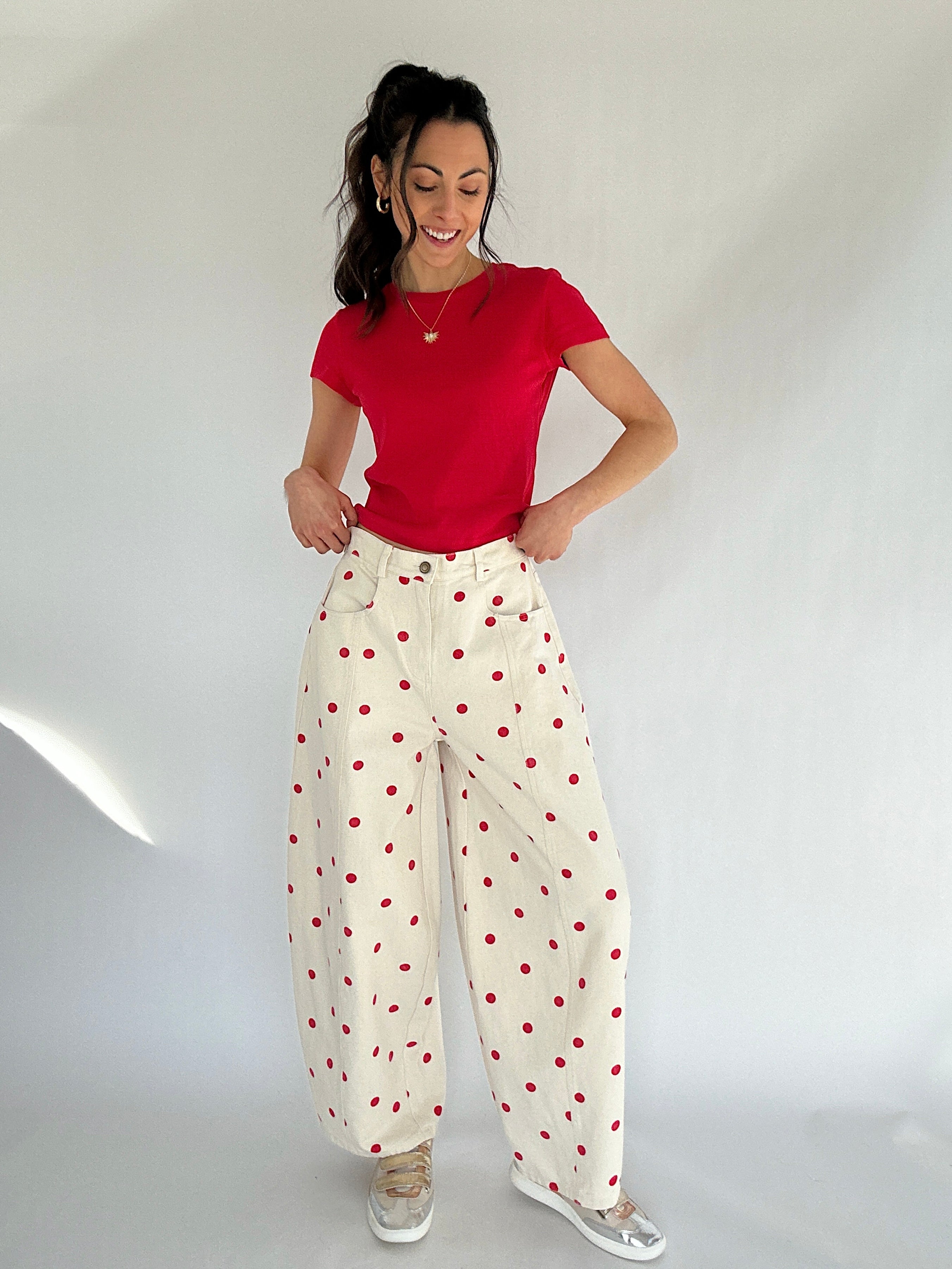 Woman wearing a red top and white pants with red polka dots on a plain background