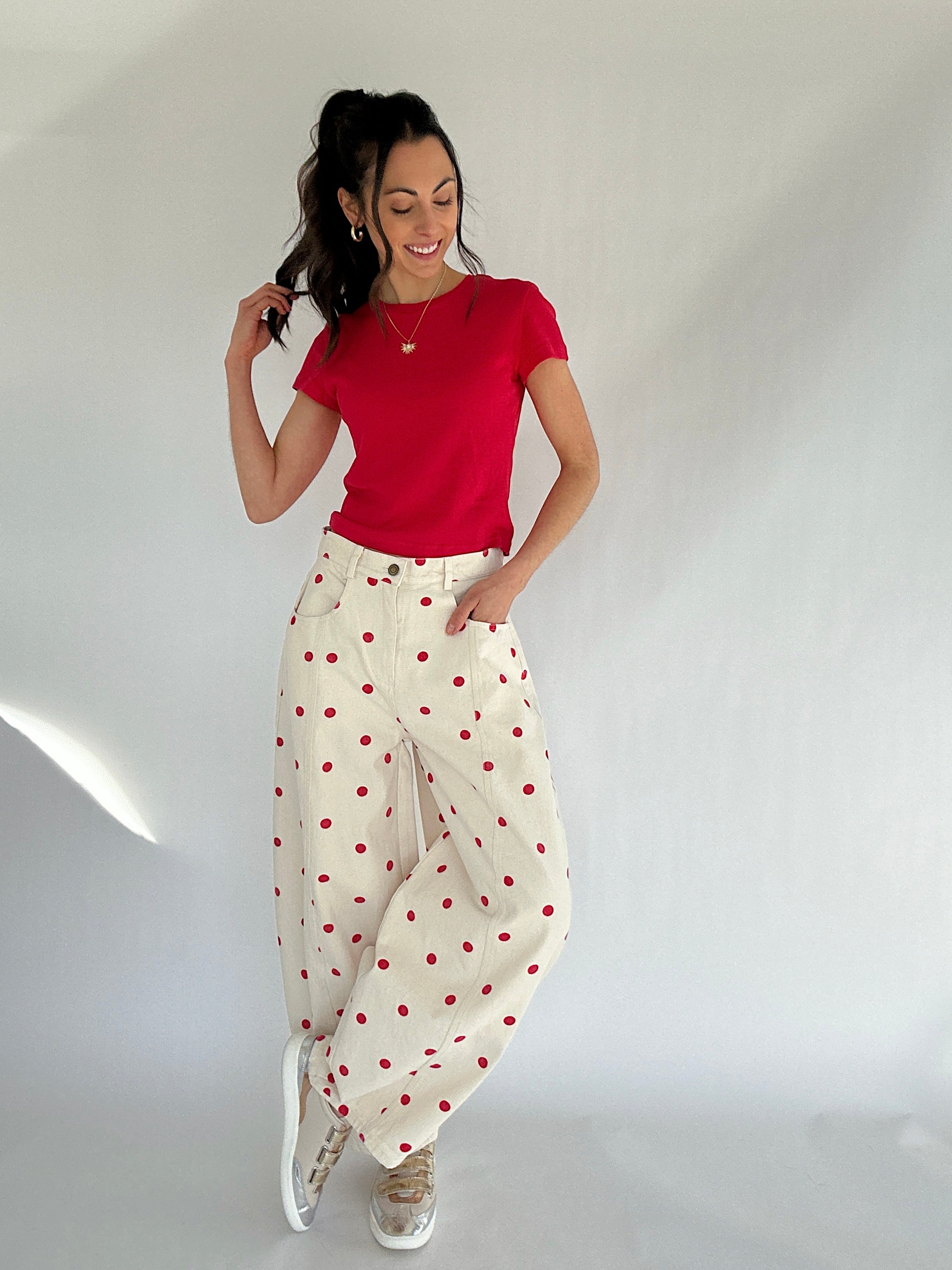 Woman wearing a red top and white pants with red polka dots against a plain background