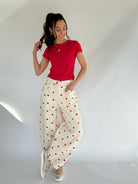 Woman wearing a red top and white pants with red polka dots against a plain background