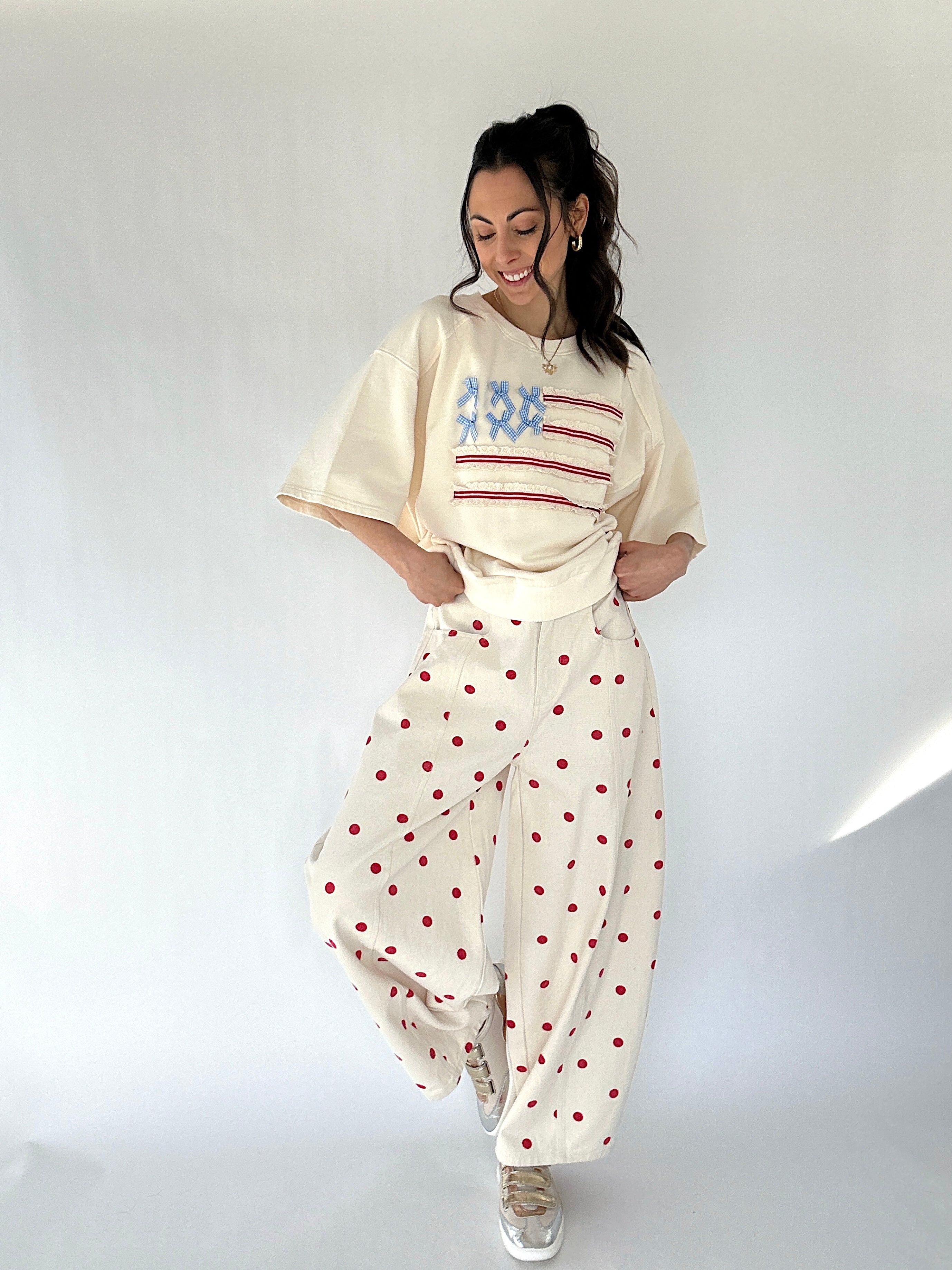Woman wearing a cream-colored top with an American flag graphic design and polka dot pants on a white background