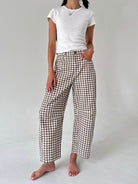 A model wearing brown and white gingham wide-leg cropped pants with a white t-shirt, standing barefoot against a light gray studio background.