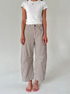 A model wearing brown and white gingham cropped wide-leg pants with a white t-shirt, standing barefoot against a light gray studio background.