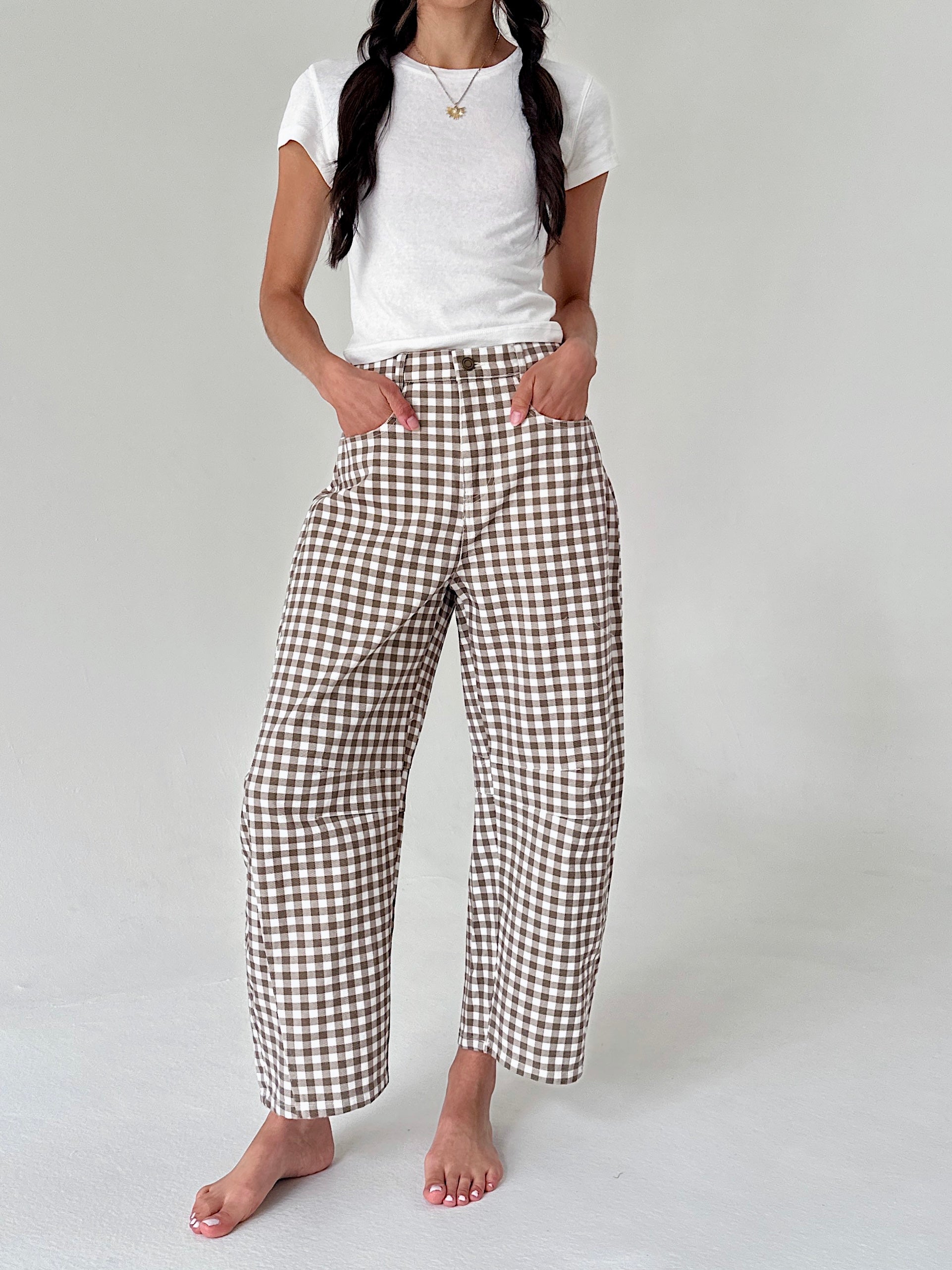A model wearing brown and white gingham cropped wide-leg pants with a white t-shirt, standing barefoot against a light gray studio background.