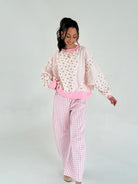 Woman wearing pink and white checkered pants and floral pullover on a plain background