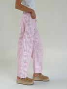 Person wearing pink checkered pants and brown shoes on a plain background from side