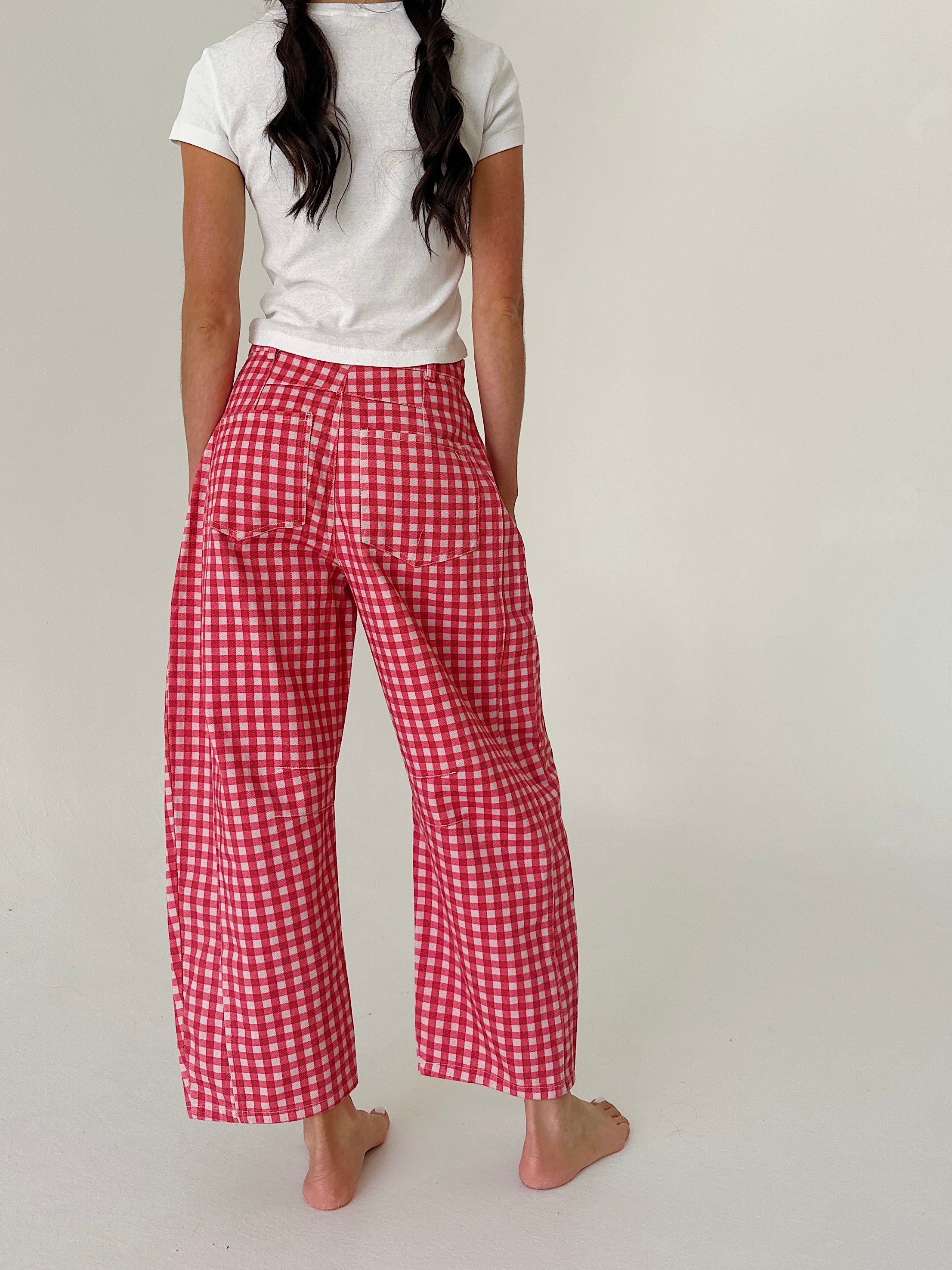 A person shown from the back wearing red and white gingham wide-leg pants, a white t-shirt, and barefoot on a plain light background.