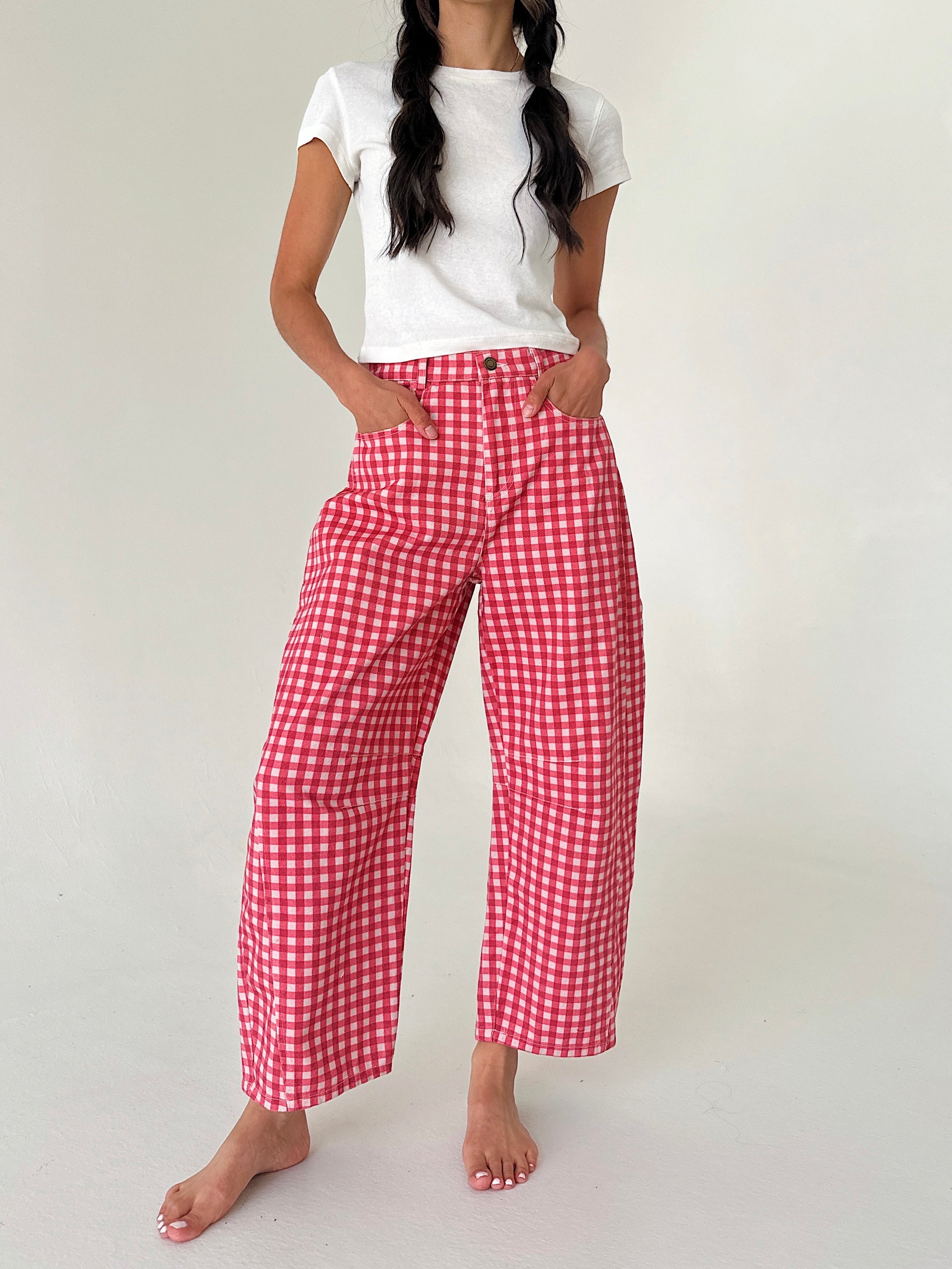 A model wearing red and white gingham cropped wide-leg pants with a white t-shirt, standing barefoot against a plain off-white studio background.