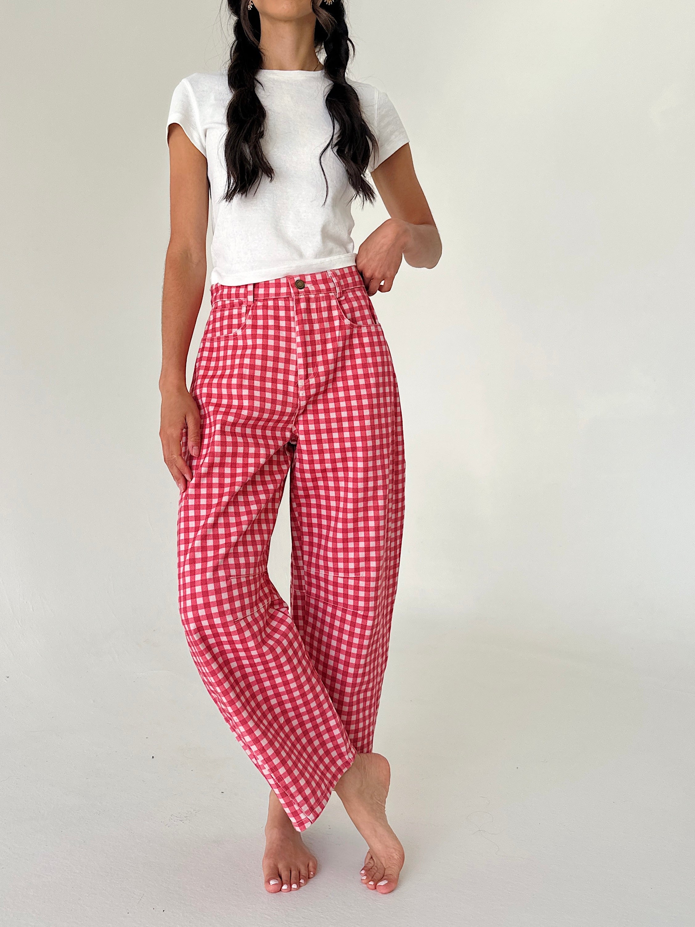 A model wearing red and white gingham wide-leg cropped pants with a white t-shirt, standing against a plain off-white studio background.