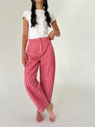A model wearing red and white gingham wide-leg cropped pants with a white t-shirt, standing against a plain off-white studio background.