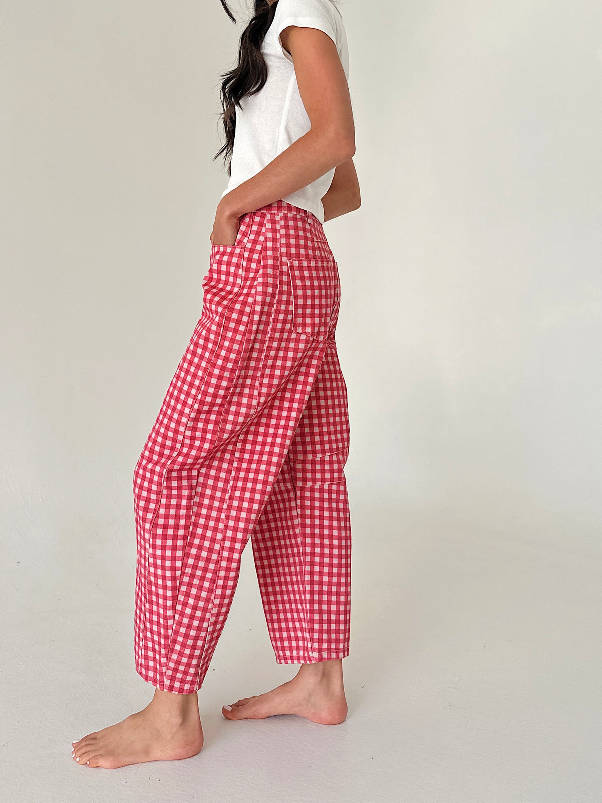 A person wearing loose red and white gingham cropped pants with a white sleeveless top, standing barefoot against a plain light background.