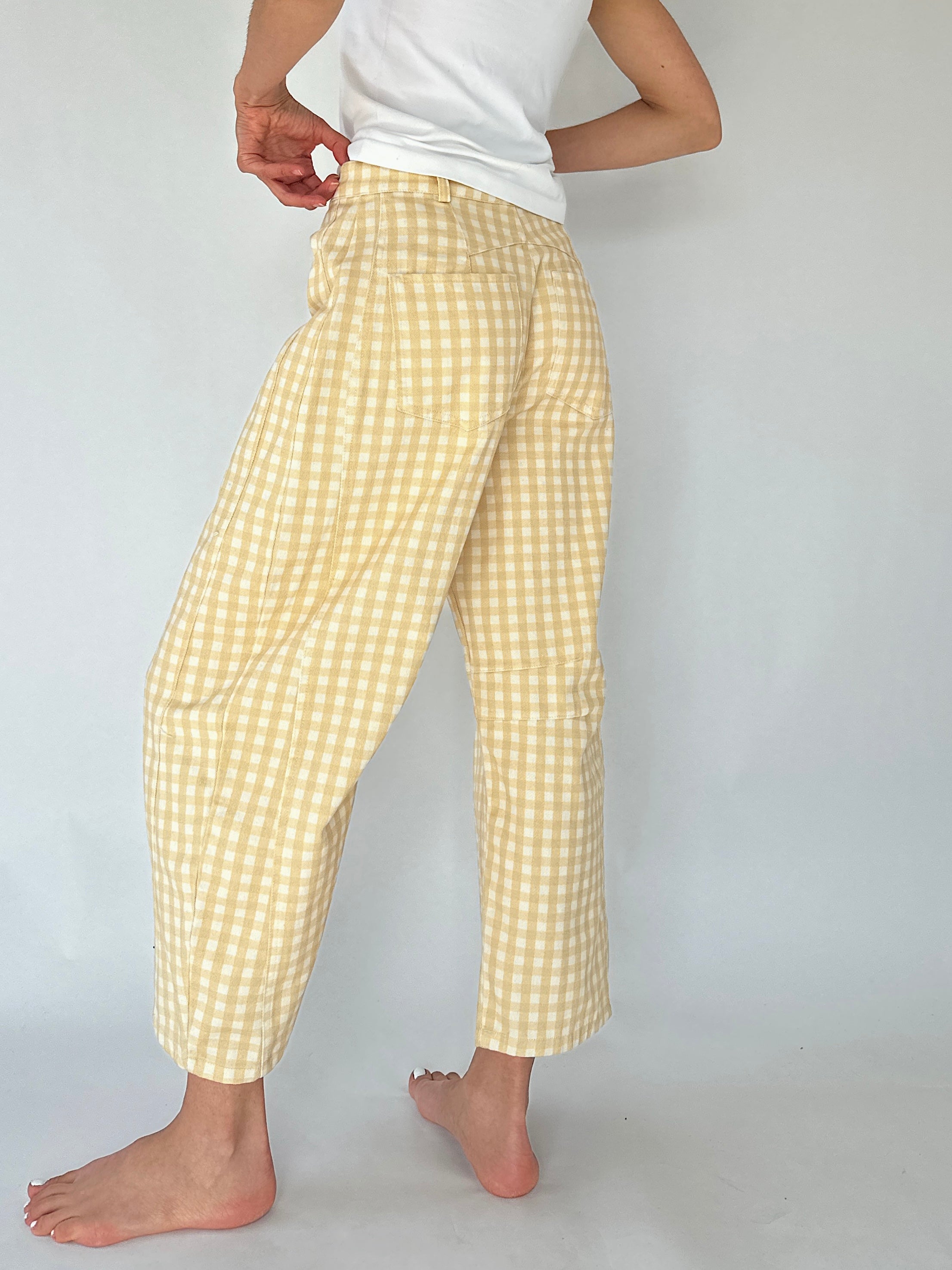 A person wearing light yellow and white gingham cropped pants with a white top, shown from the waist down against a plain light gray studio background.