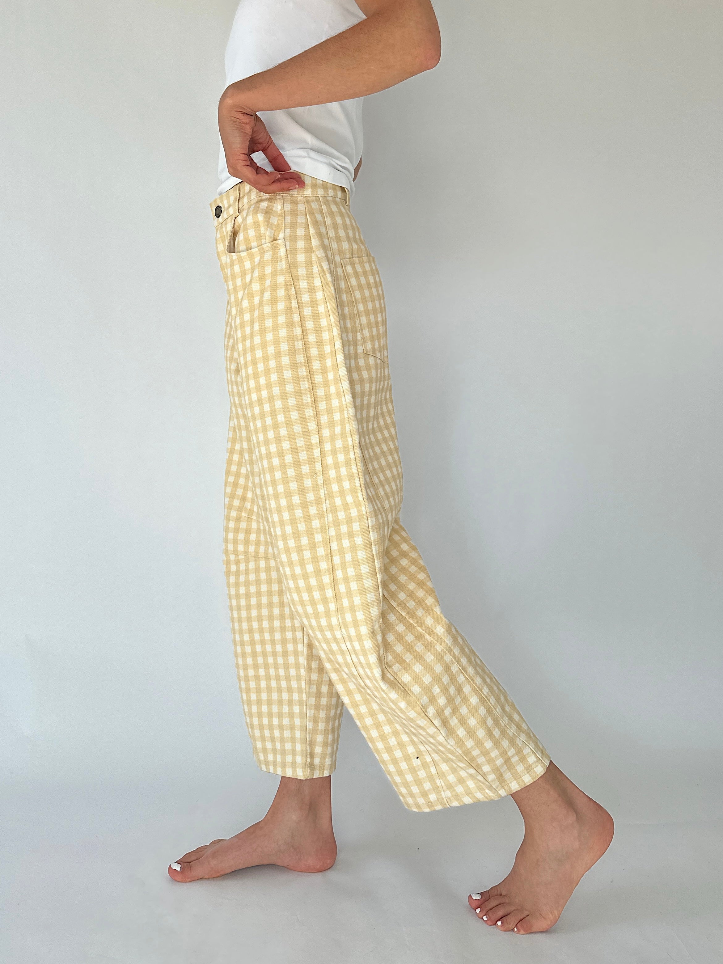 A person wearing loose, barrel cropped pants in a pale yellow and white gingham check pattern, paired with a white top, shown from the waist down against a light gray studio background.