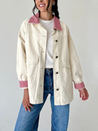 A woman wearing a cream-colored utility jacket with red and white gingham patterned collar and cuffs, paired with a white t-shirt and blue jeans.