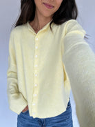 Person wearing a light yellow cardigan with a plain background