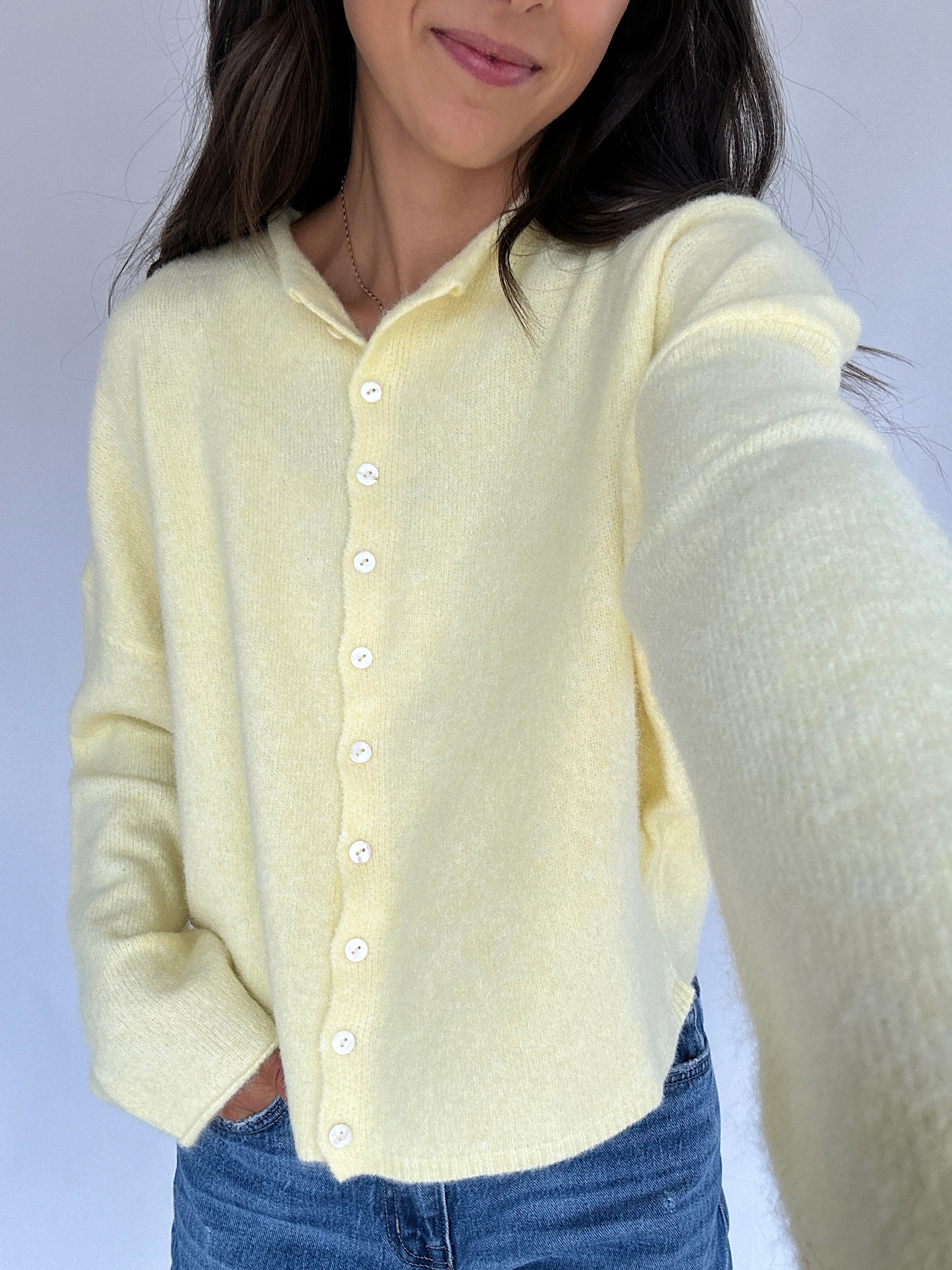 Person wearing a light yellow cardigan with a plain background