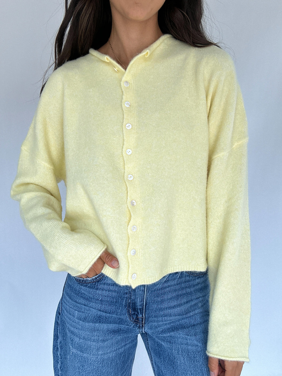 Person wearing a light yellow cardigan over a blue top against a plain background