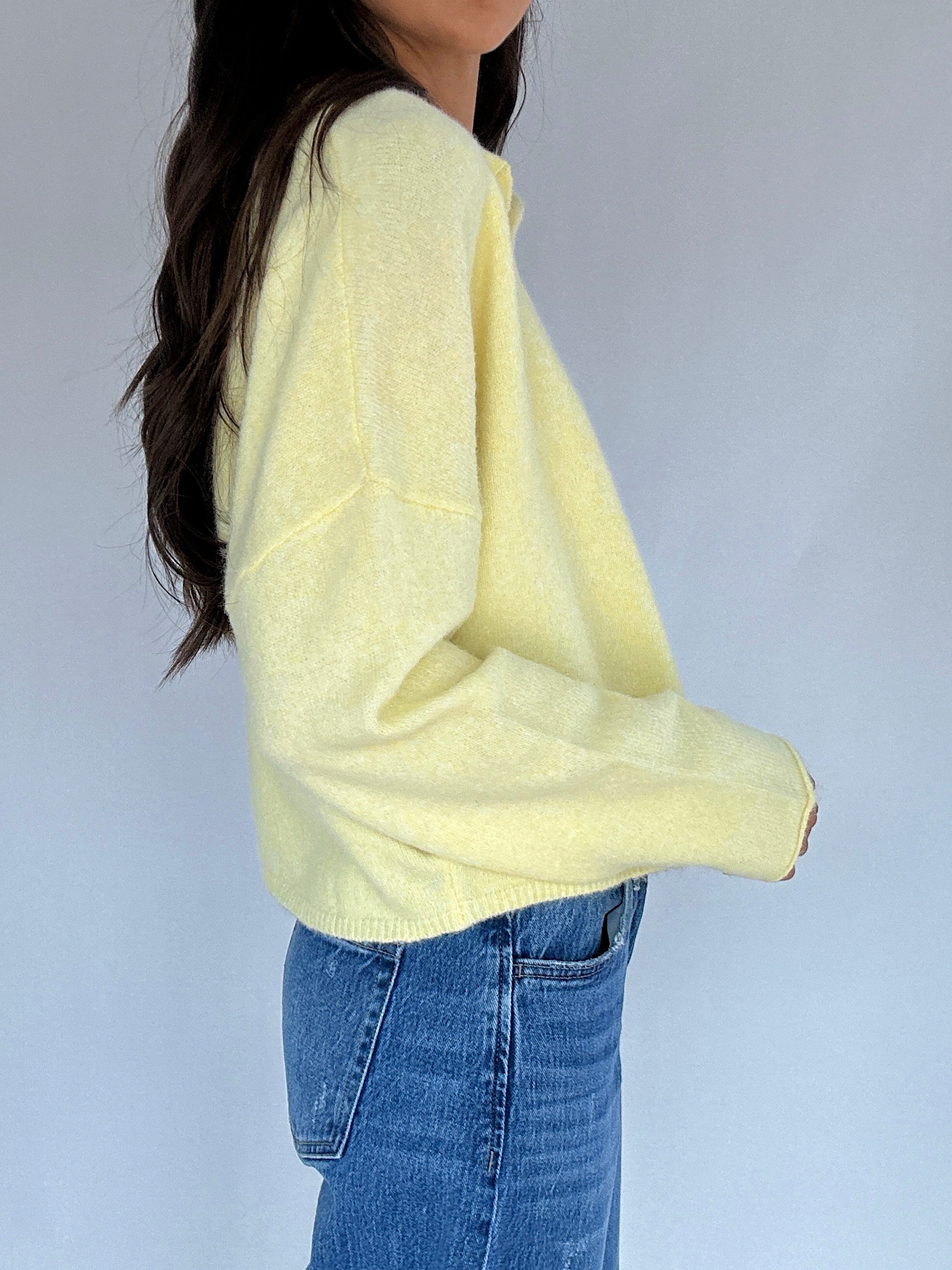 Person wearing a light yellow sweater and blue jeans against a plain background