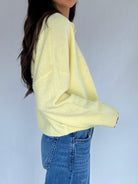 Person wearing a light yellow sweater and blue jeans against a plain background