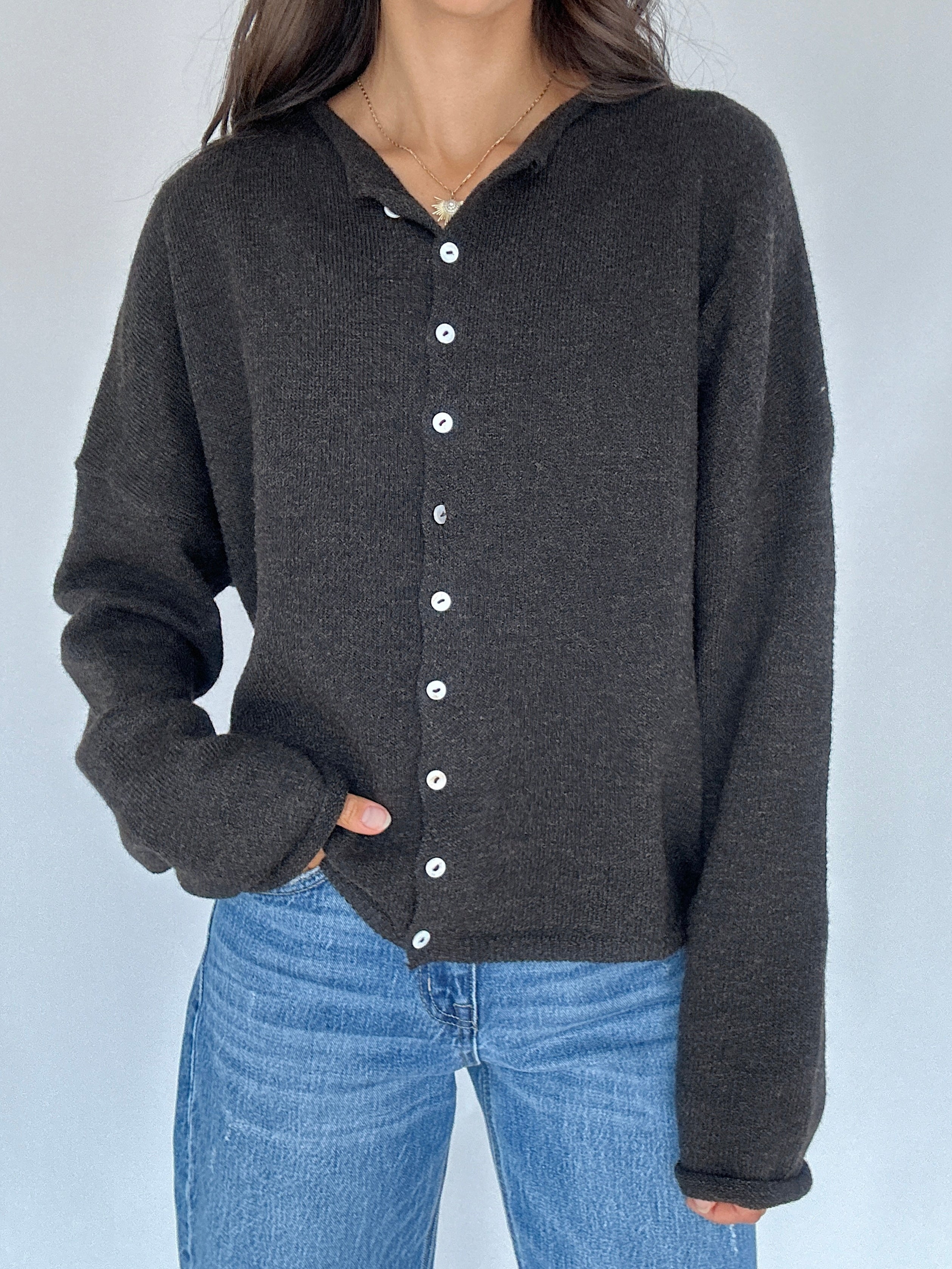 Person wearing a dark chocolate button-up cardigan over blue jeans against a light gray background