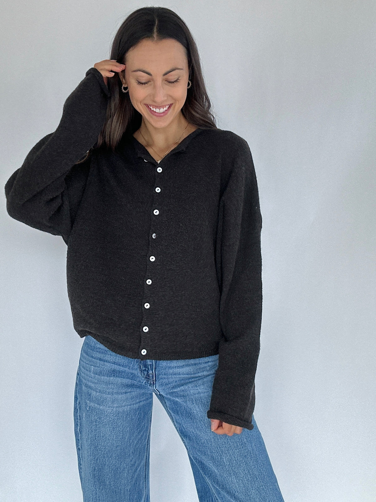 Woman wearing a black cardigan and blue jeans against a white background