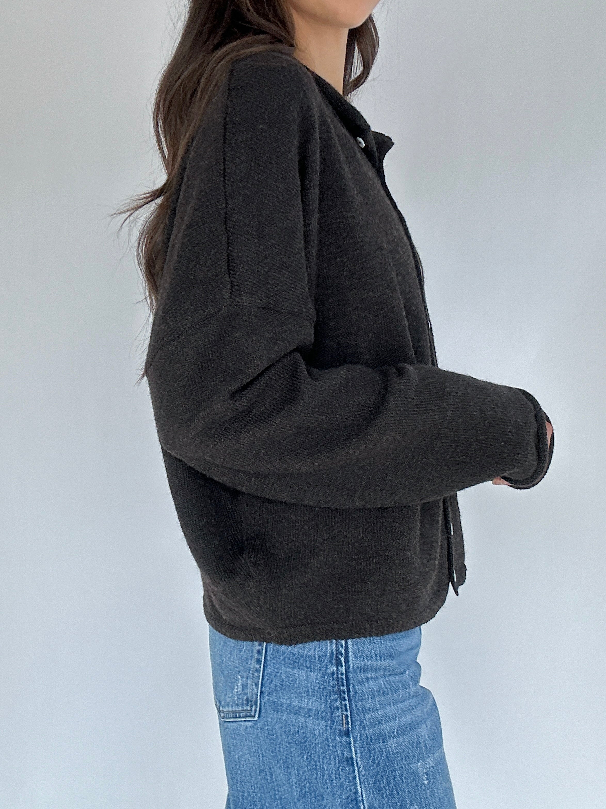 Person wearing a dark gray cardigan and blue jeans against a white background