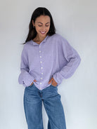 Woman wearing a light purple button-up cardigan and blue jeans against a white background