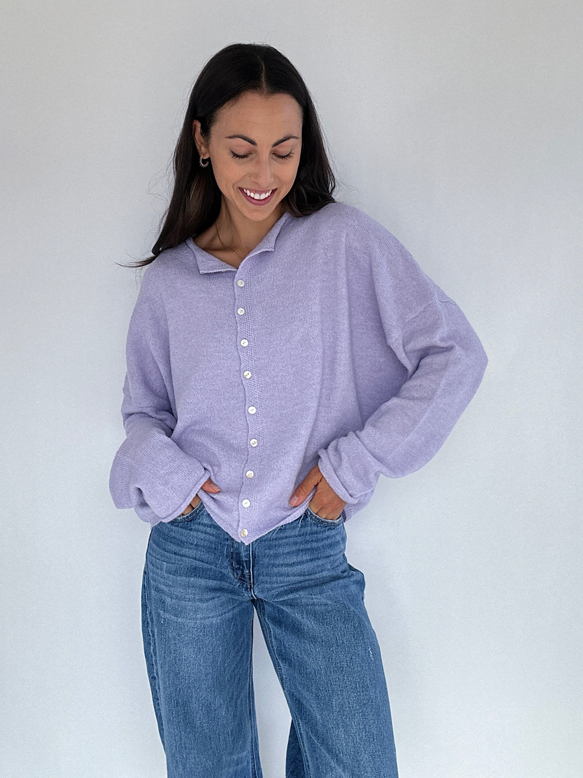 Woman wearing a light purple button-up cardigan and blue jeans against a white background