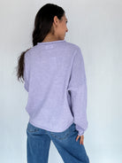 Person wearing a light purple sweater and blue jeans against a white background