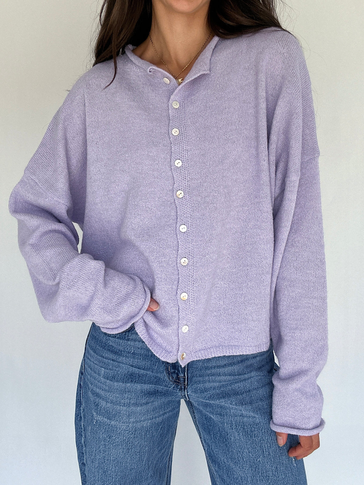 Person wearing a light purple button-up shirt and blue jeans against a plain background