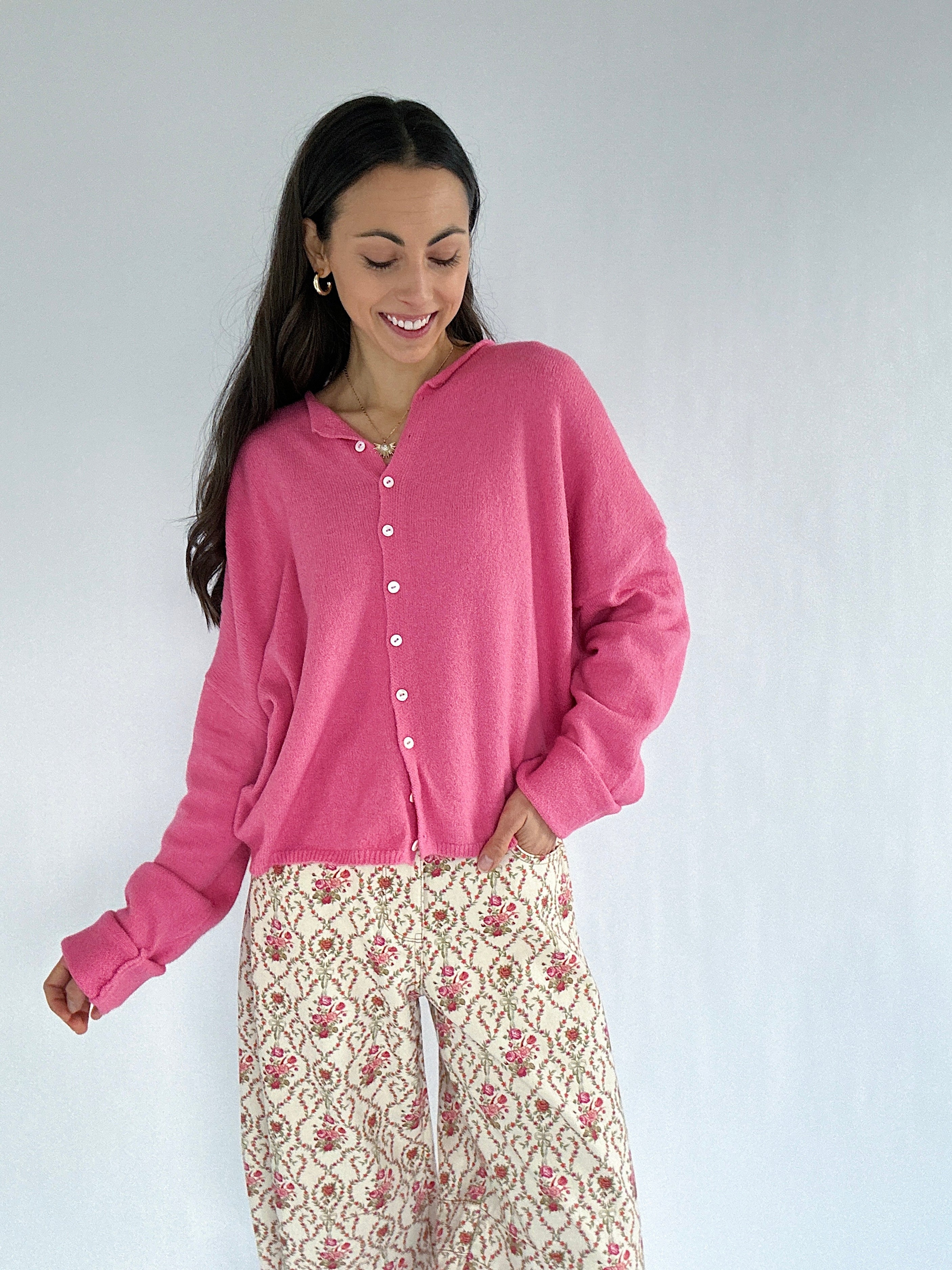 Woman wearing a pink cardigan with floral patterned pants against a white background