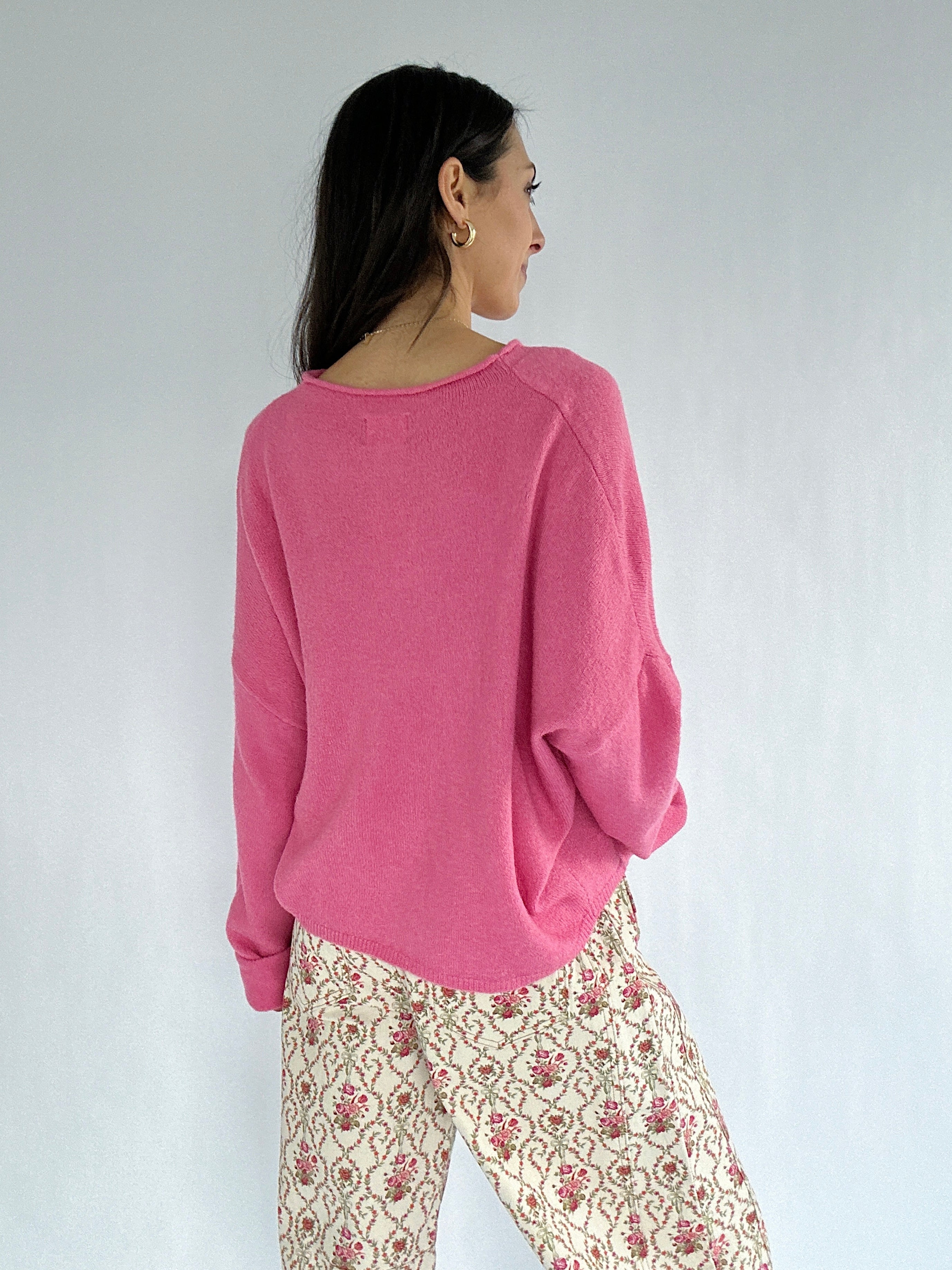Woman wearing a pink sweater and patterned pants against a white background showing the back
