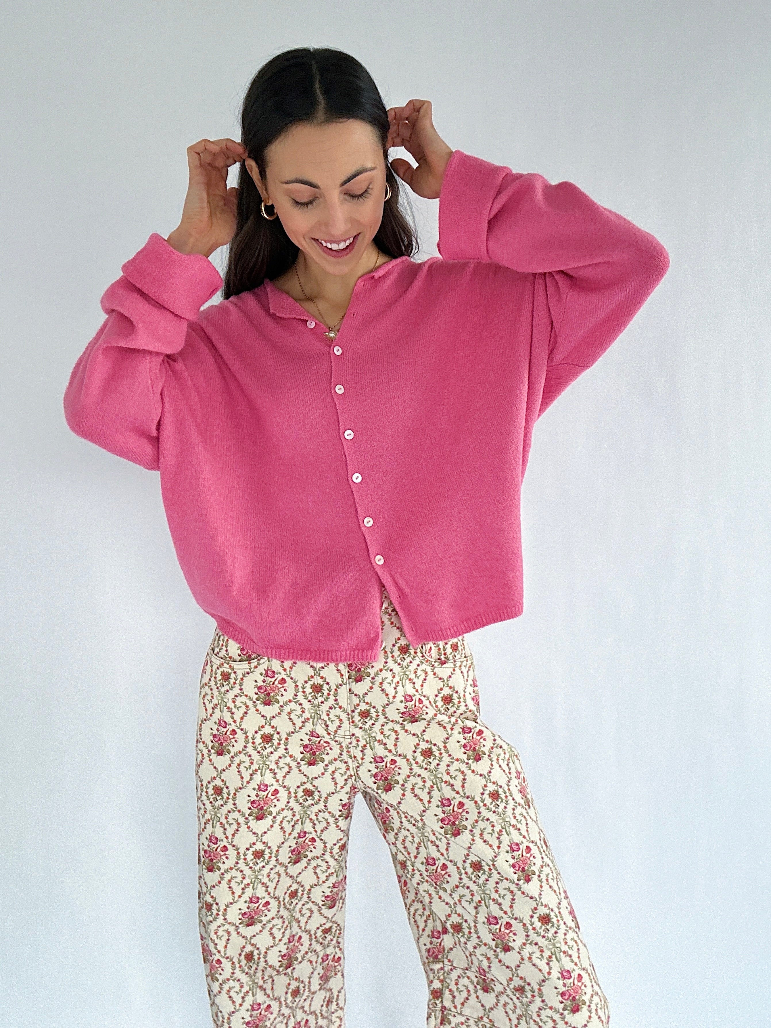 Woman wearing a pink cardigan and floral pants against a white background