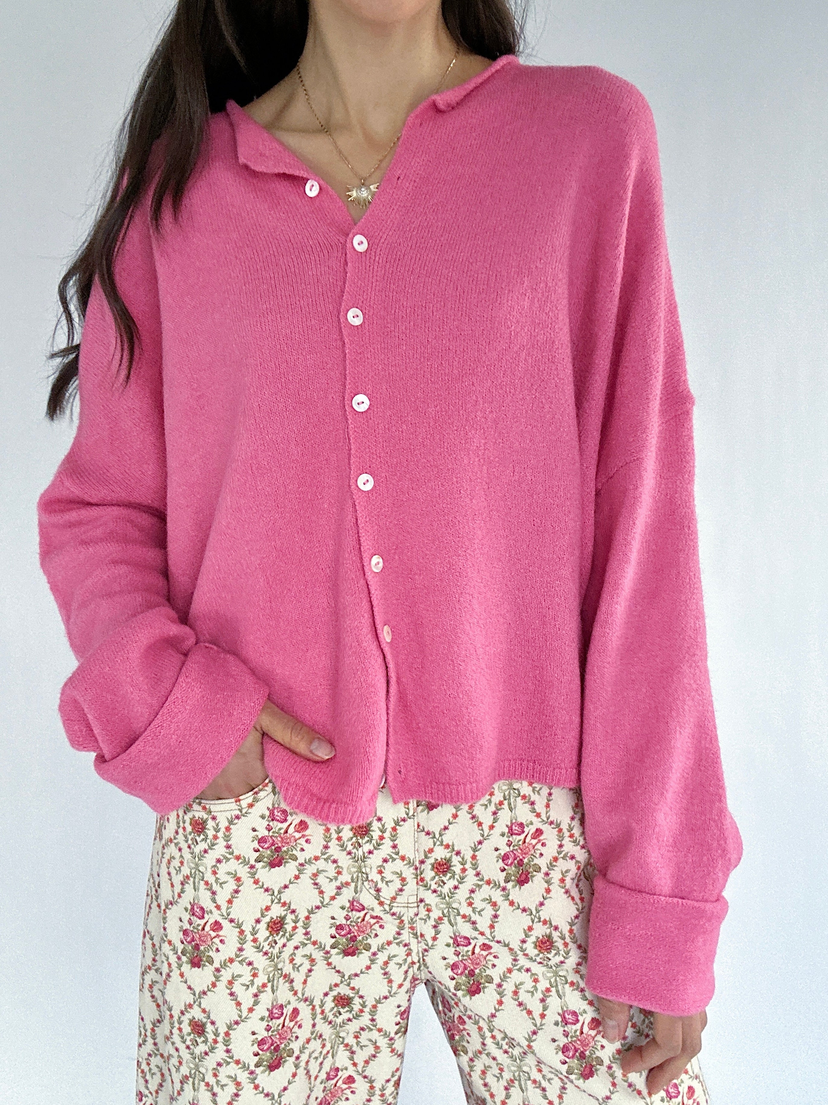 Person wearing a pink cardigan with a floral pair of pants on a plain background