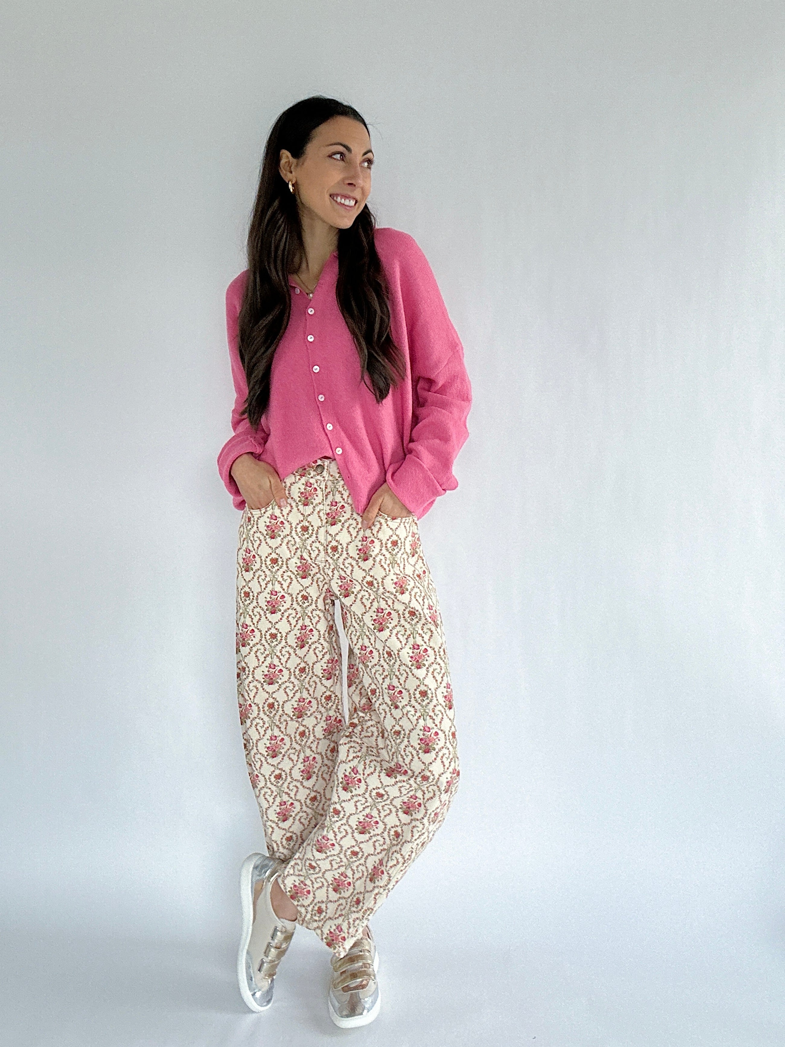 Woman wearing a pink cardigan and floral pants against a white background
