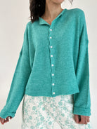 Person wearing a teal cardigan over a floral outfit on a plain background
