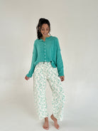 Woman wearing a teal cardigan and floral pants on a white background