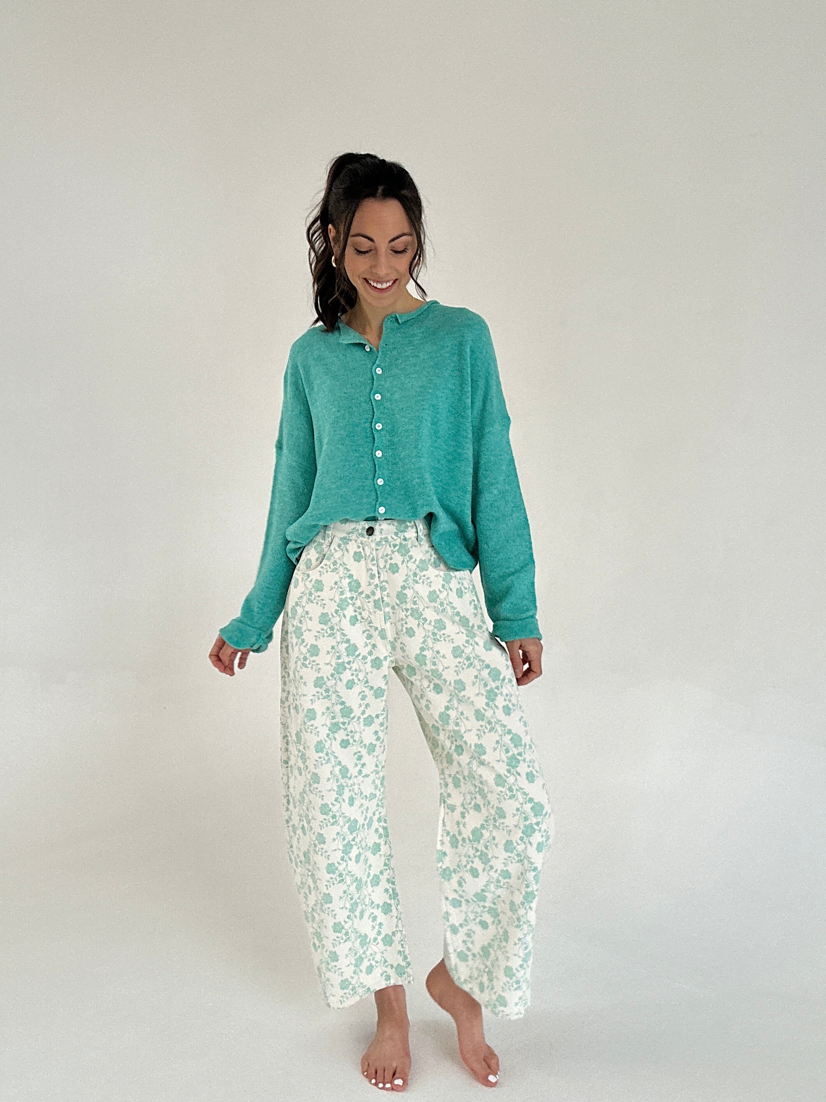 Woman wearing a teal cardigan and floral pants on a white background