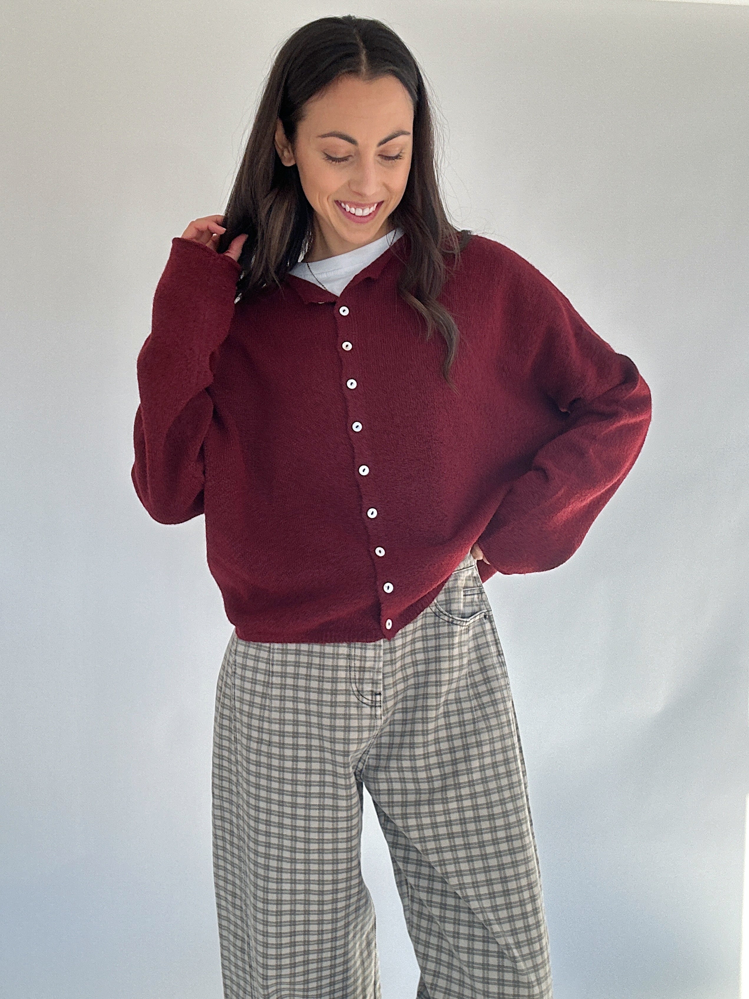 Woman wearing a burgundy cardigan over a white shirt with plaid pants on a plain background