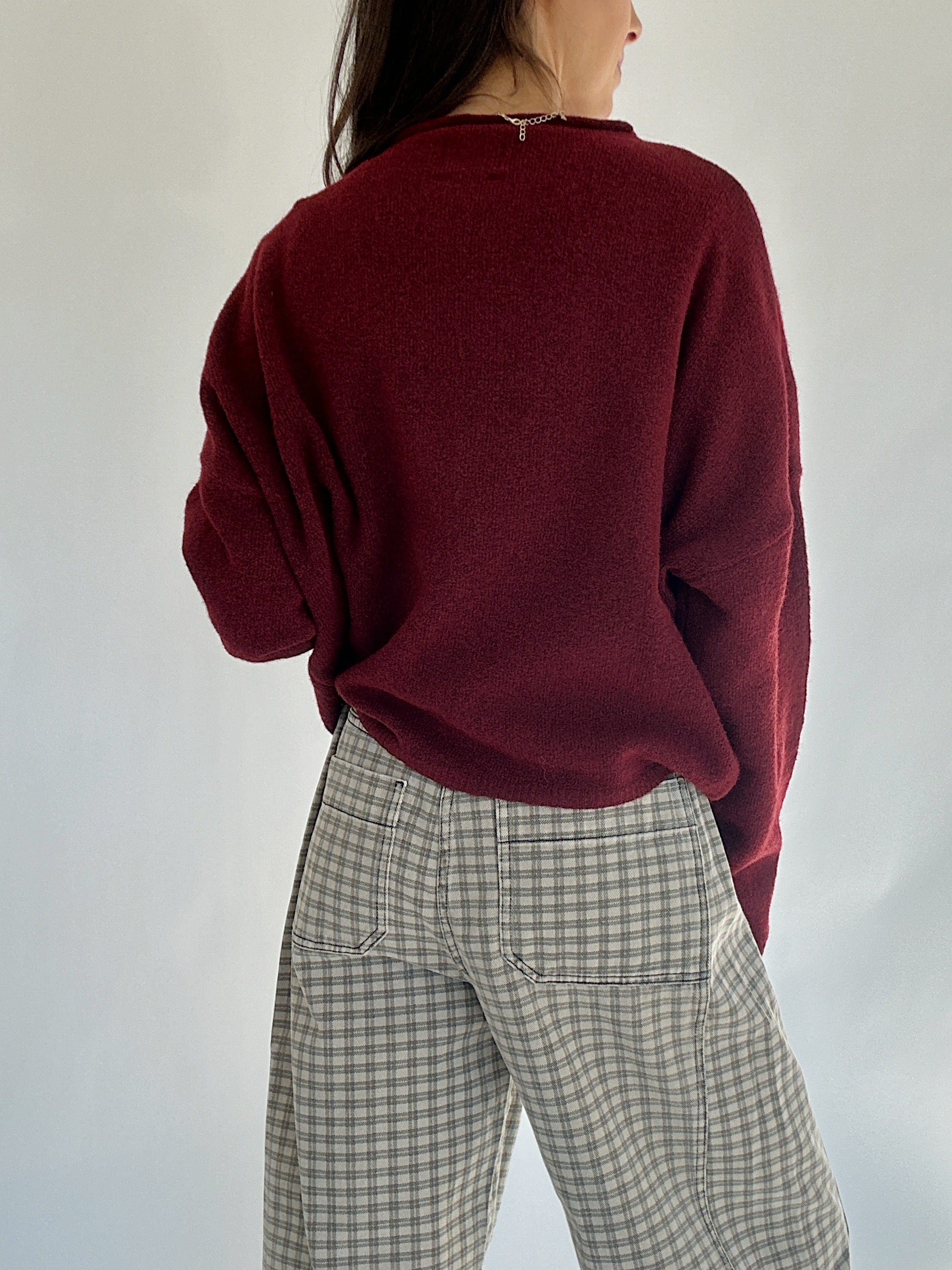 Person wearing a burgundy sweater and plaid pants against a plain background back view