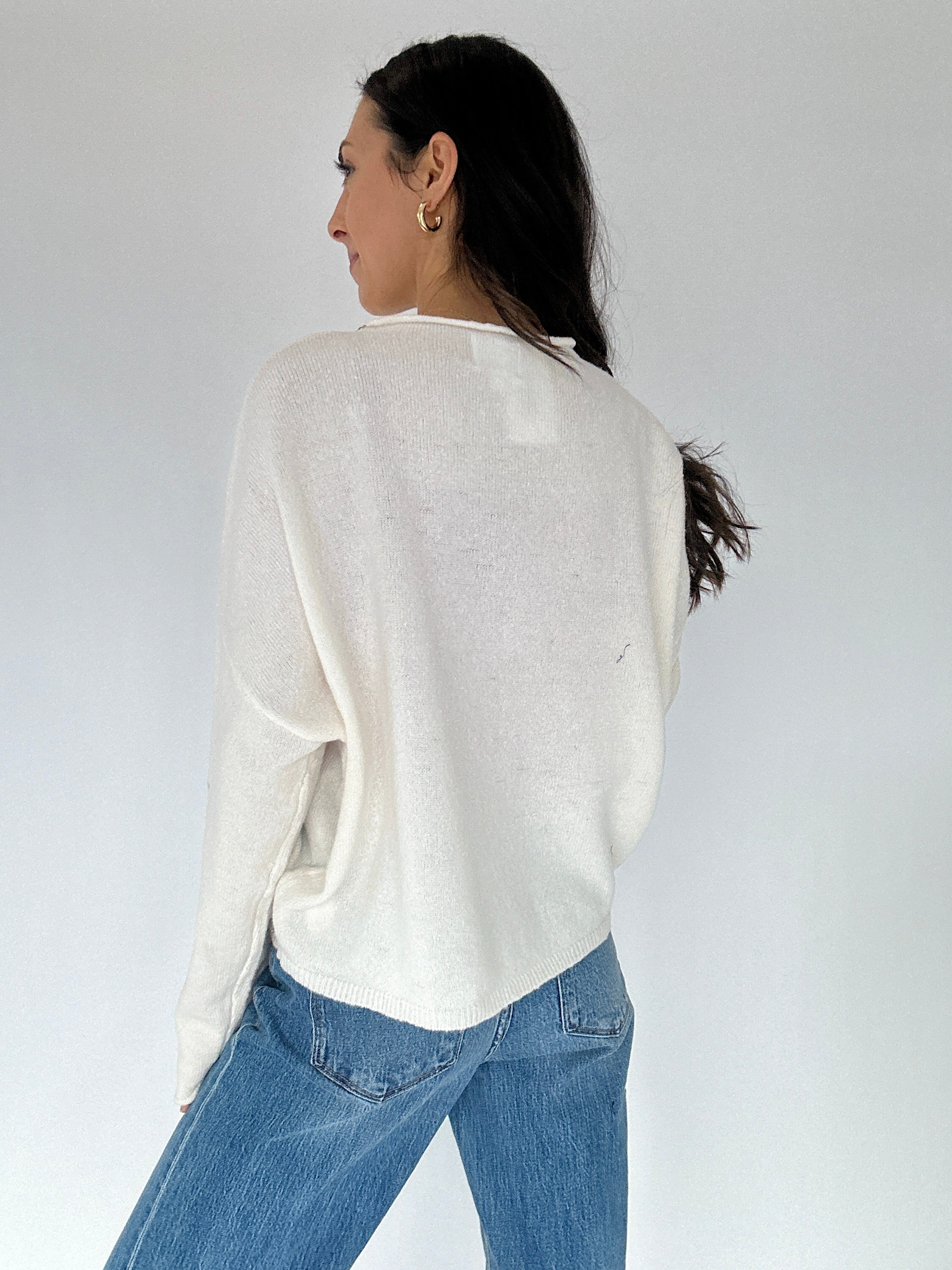 Person wearing a white sweater and blue jeans against a plain background from back