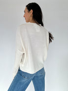 Person wearing a white sweater and blue jeans against a plain background from back