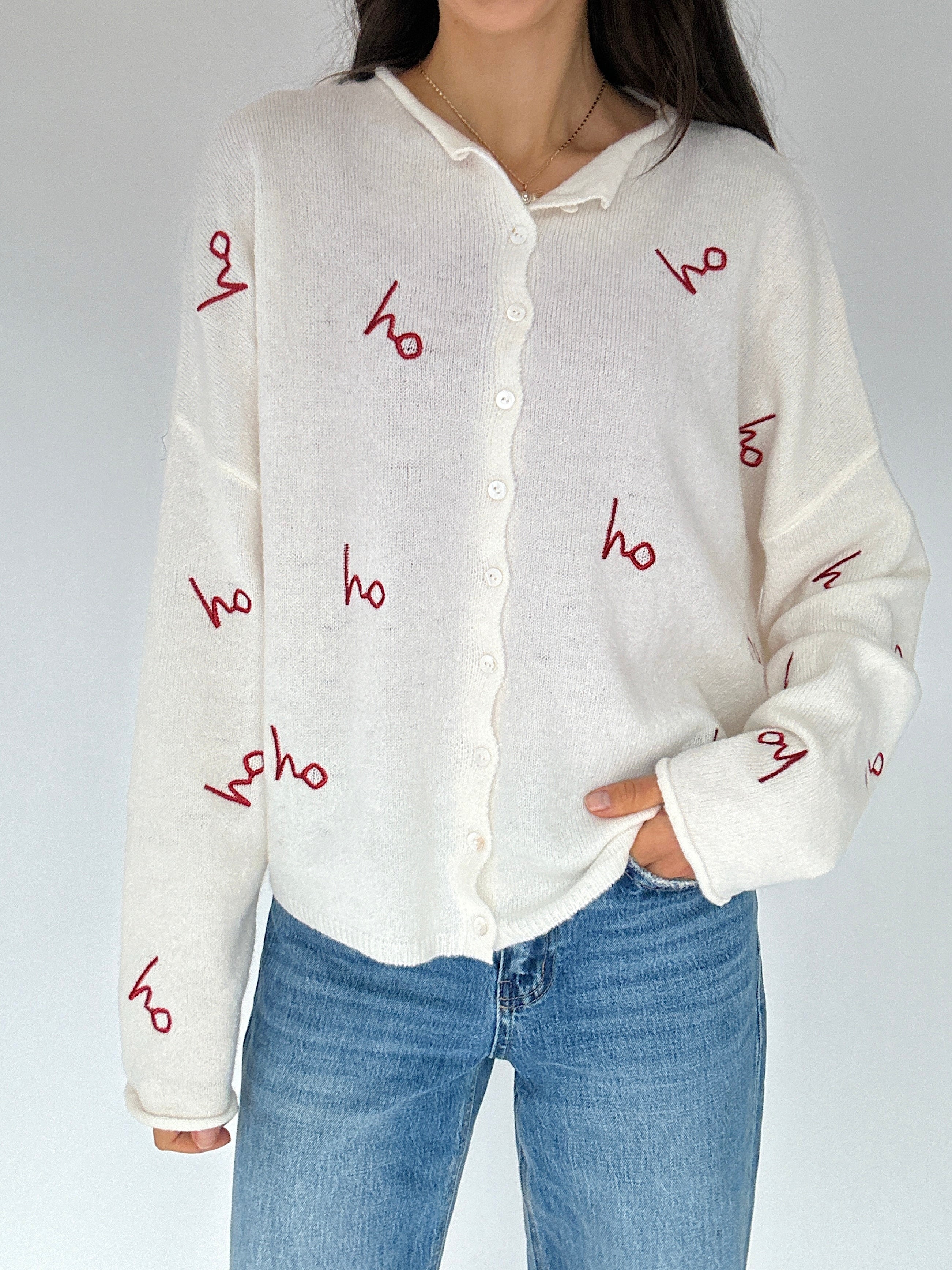 Person wearing a white sweater with red 'ho ho ho' text and blue jeans on a plain background